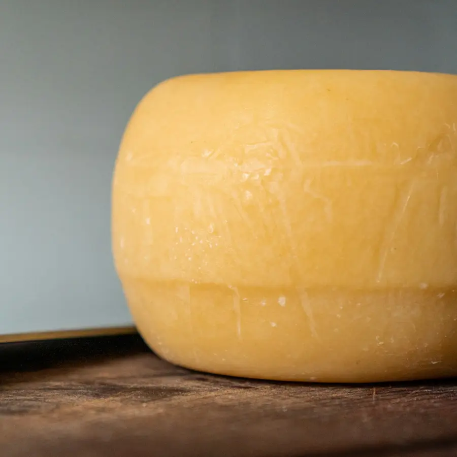 Een hele ronde jonge kaas op een houten tafel